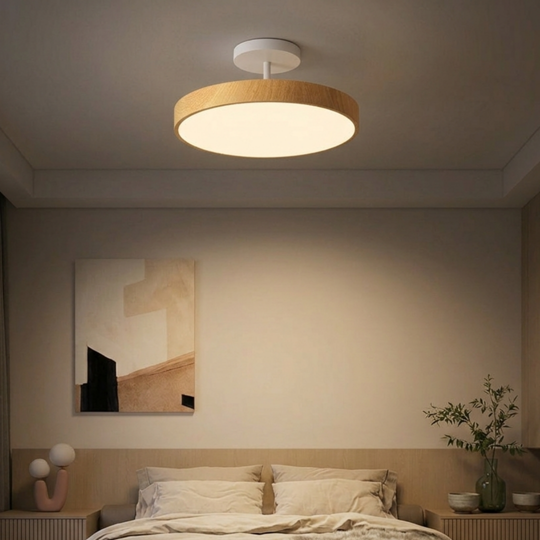 Lamp met lichte houtlook rand en witte steun boven een bed in een rustige slaapkamer met beige tinten. 7