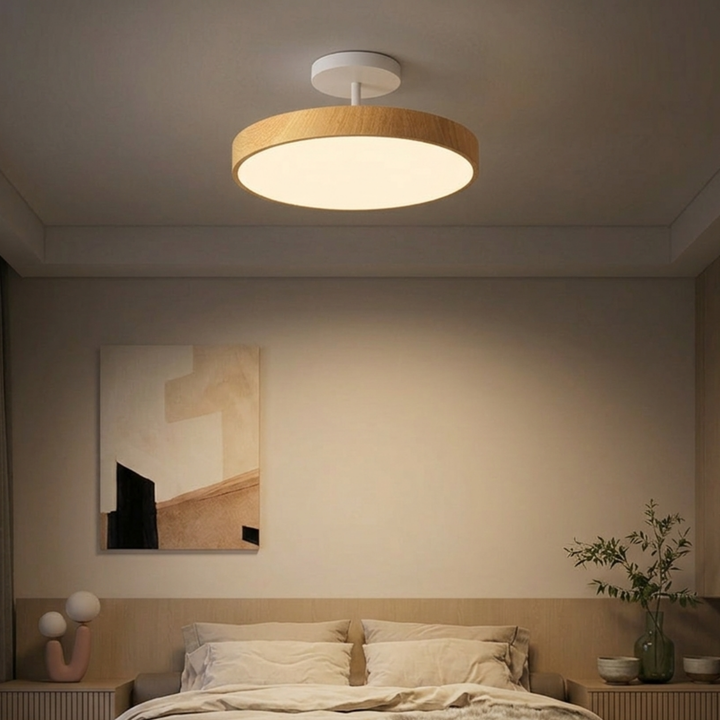 Lamp met lichte houtlook rand en witte steun boven een bed in een rustige slaapkamer met beige tinten. 7