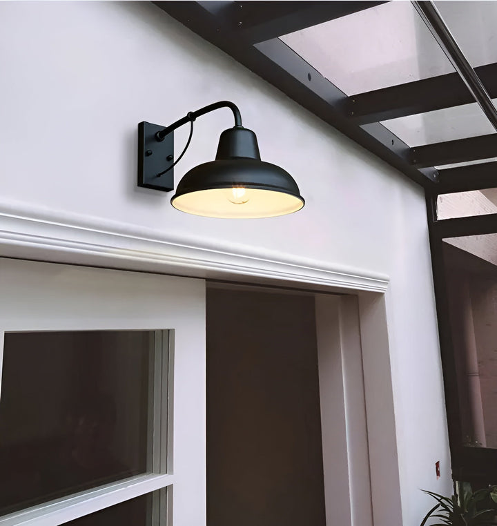 Zwarte wandlamp met witte binnenzijde van de kap, aan een witte gevel boven een deuropening, met brandende gloeilamp. 4