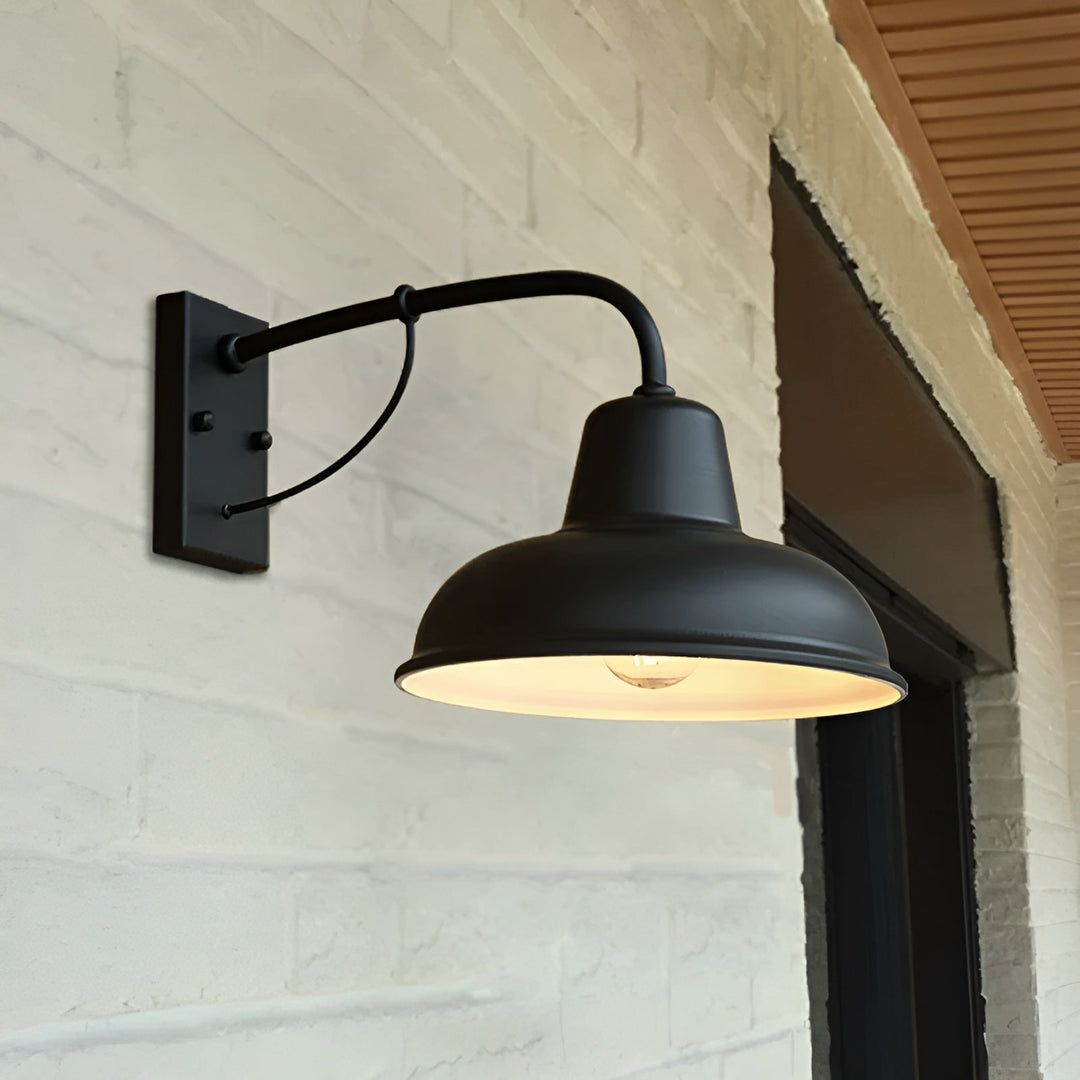 Zwarte wandlamp met brandende lamp tegen een witgeschilderde bakstenen muur naast een donkere deuropening, schuin van onderen gezien. 5