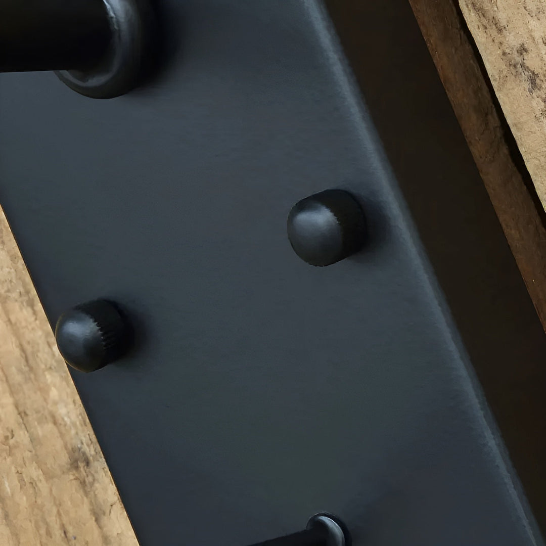 Close-up van de rechthoekige zwarte montageplaat met twee bolle klinknagels, gemonteerd tegen een houten ondergrond. 7