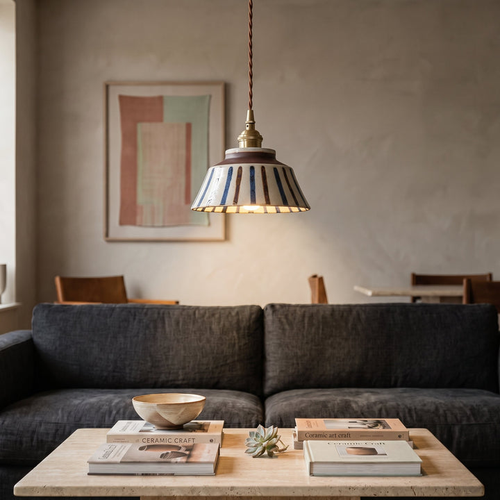 Gestreepte keramische hanglamp boven een salontafel met boeken, een aardewerk kom en een vetplant, voor een donkere bank. 5