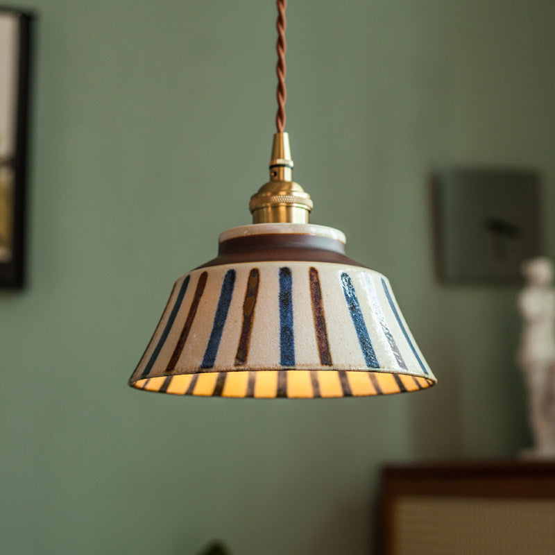 Hanglamp met keramische kap met blauwe en bruine verticale strepen, messing fitting en gevlochten snoer voor een groene muur. 3