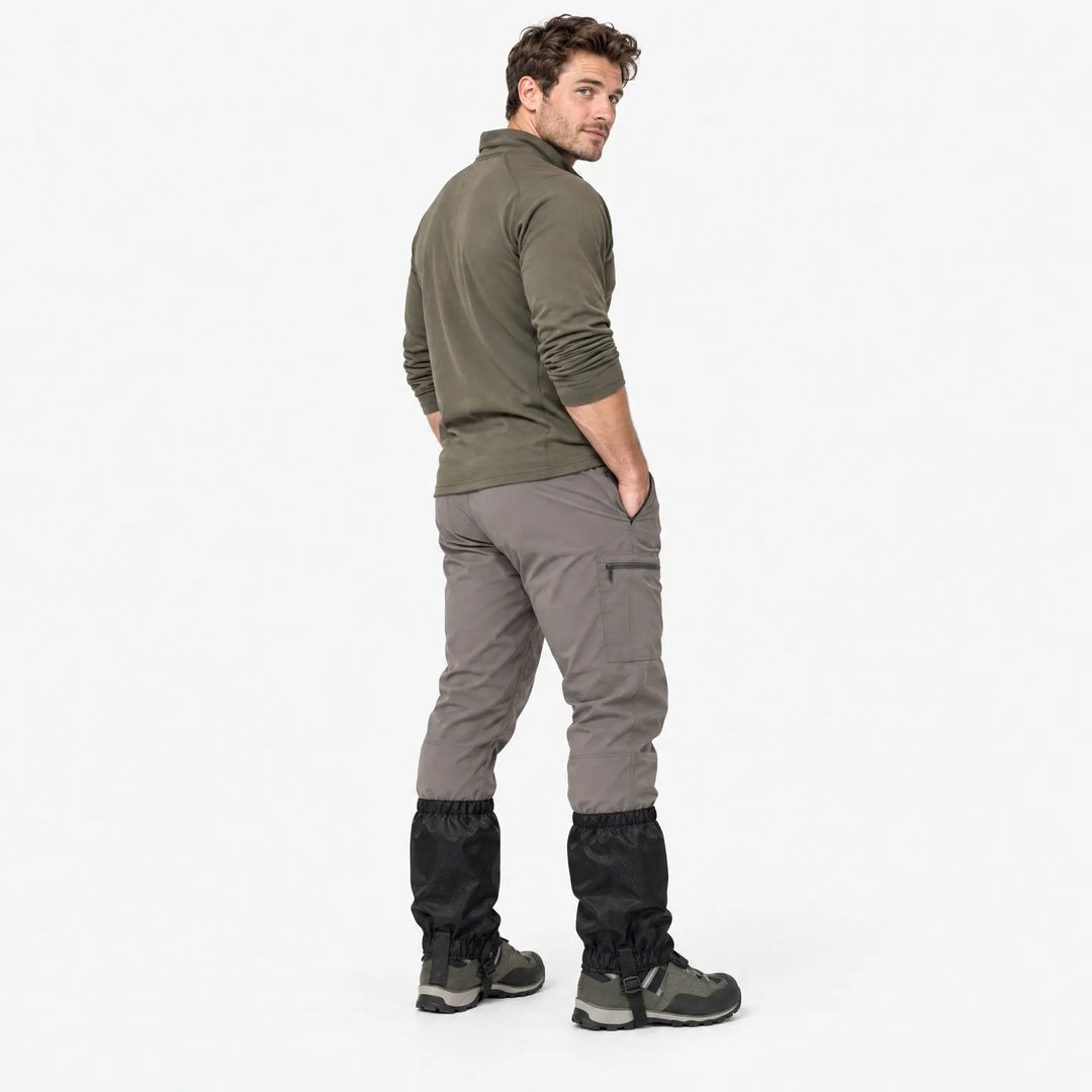 Wandelaar met zwarte gamaschen over grijze broek en wandelschoenen, van achteren gezien en over de schouder kijkend. 4