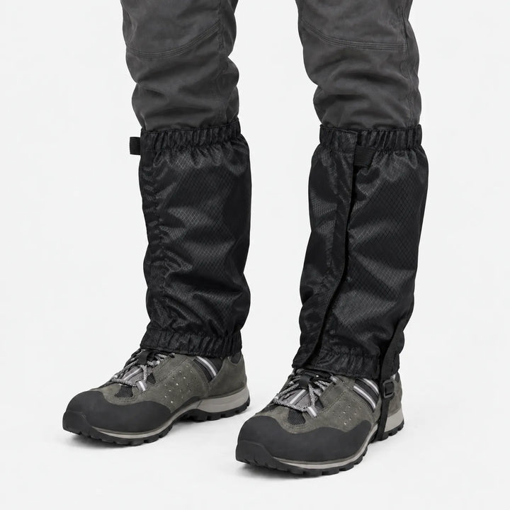 Zwarte gamaschen met ruitjesstructuur, gedragen over grijze wandelschoenen en donkere broek op een witte achtergrond. 9
