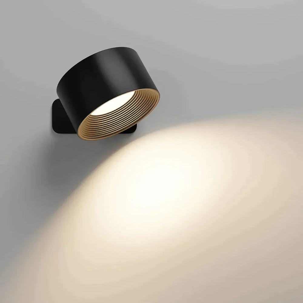 Zwarte ronde wandlamp met goudkleurige gegroefde binnenkant die een warme lichtbundel op de muur werpt. 2