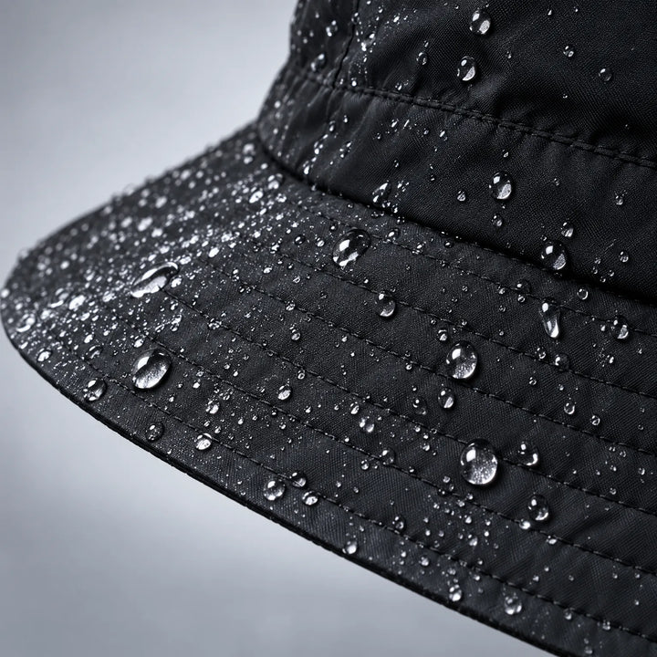 Close-up van de rand van een zwarte bucket hoed met veel waterdruppels op de stof en de stiksels. 6