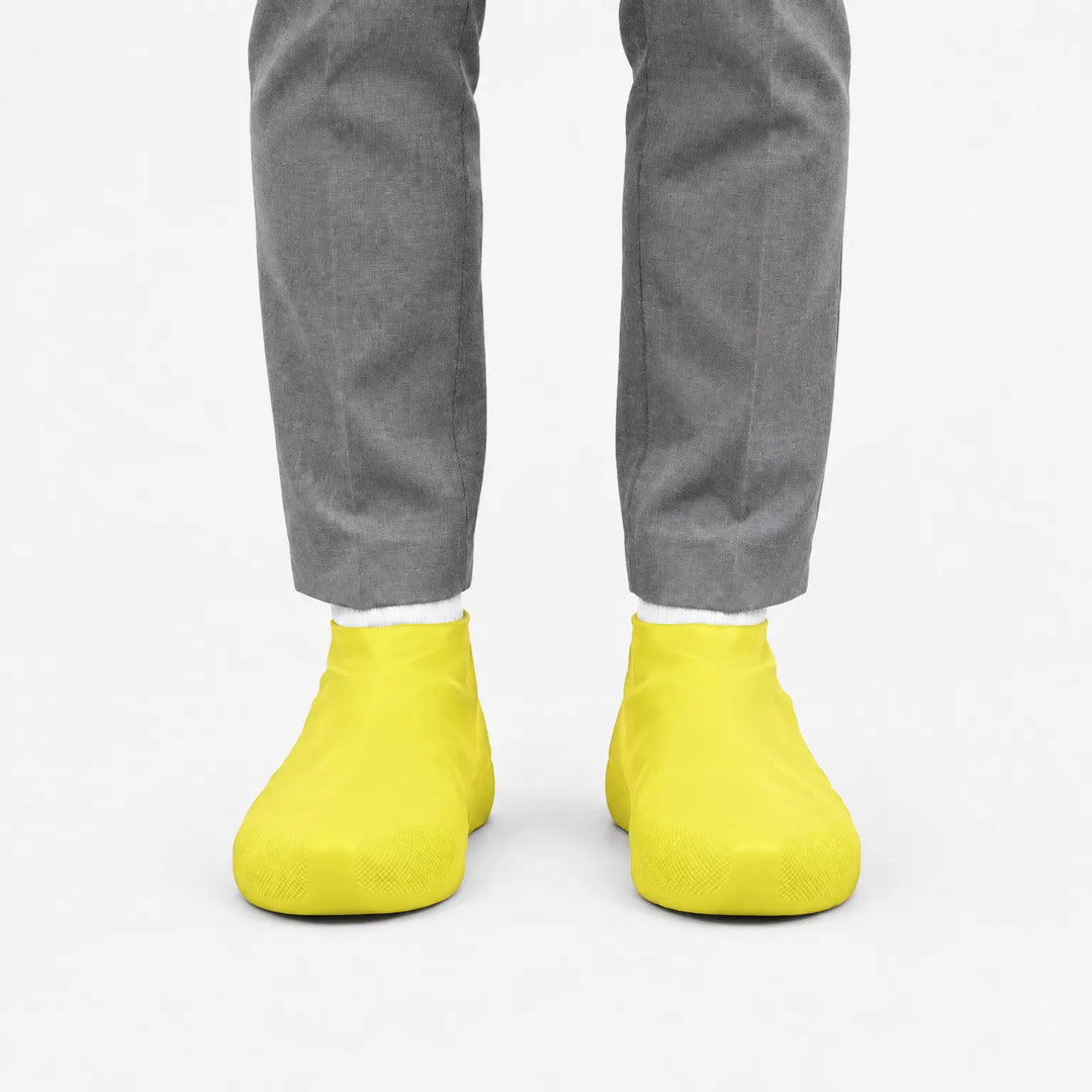 Voorkant van gele overschoenen aan de voeten van iemand in een grijze pantalon, op een witte achtergrond. 7