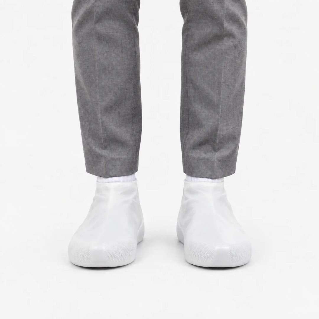 Voorkant van witte, doorschijnende overschoenen met profiel op de neus, gedragen met een grijze pantalon. 8