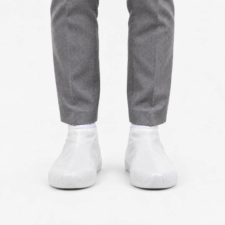 Voorkant van witte, doorschijnende overschoenen met profiel op de neus, gedragen met een grijze pantalon. 8