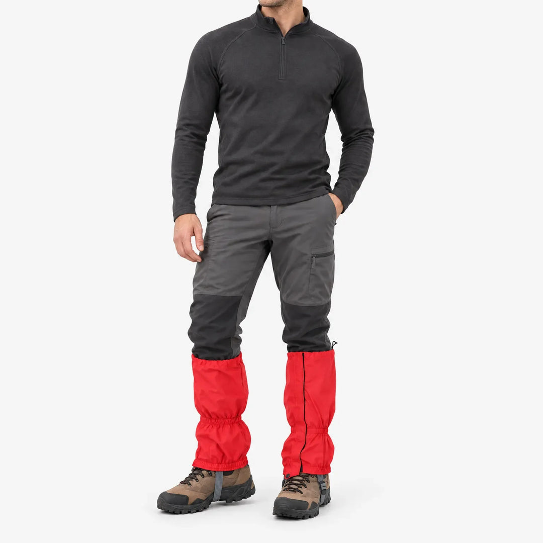 Man in donkere trui en grijze wandelbroek draagt rode gaiters met rits aan de zijkant, op witte achtergrond. 2