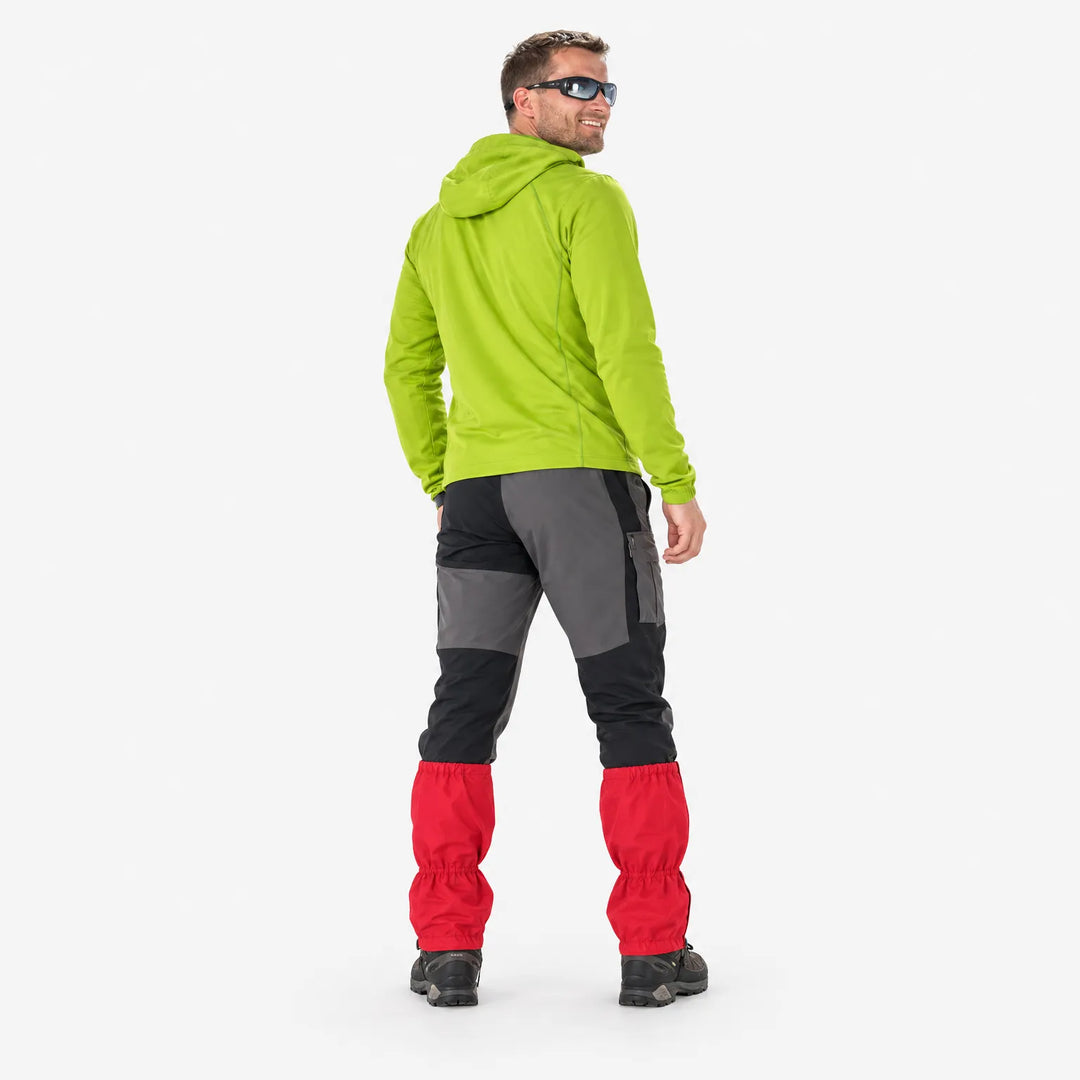 Achteraanzicht van een man in groene hoodie die over zijn schouder lacht, met rode gaiters over zijn wandelbroek. 4