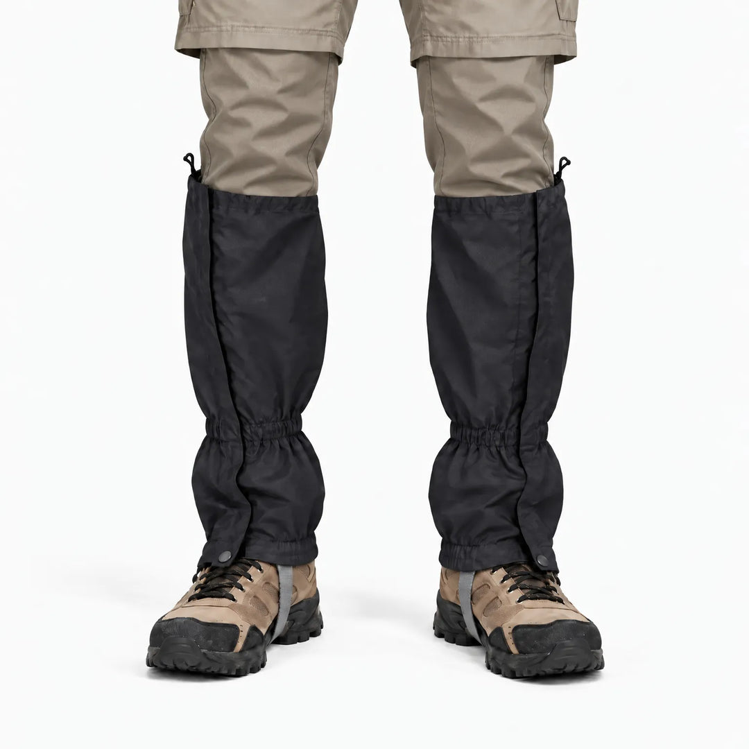 Voorkant van zwarte gaiters over een beige broek en wandelschoenen, met elastische enkelrand en drukknoop. 9