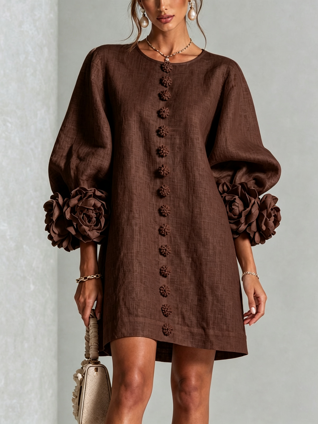 Voorkant van donkerbruine mini-jurk met pofmouwen, rij bloemknopen en grote rozenmanchetten, gedragen met parelkettinkje en handtasje. 27
