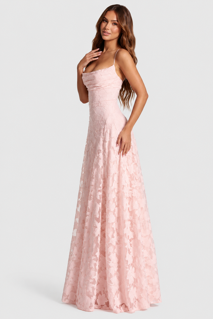 Roze jurk met bloemenkant en gedrapeerde halslijn, gedragen door een model in driekwartzijaanzicht met een hand op de borst. 1