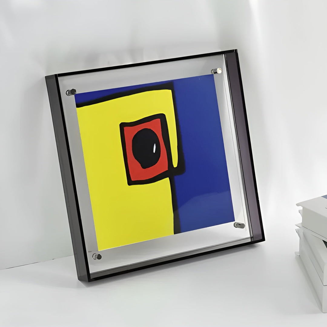 Vierkante acrylfotolijst met donkere rand en metalen bevestigingsstiftjes, schuin tegen een witte wand geplaatst met een kleurrijk abstract kunstwerk erin. 6