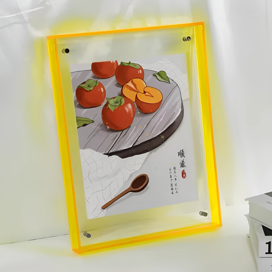 Neon gele acrylfotolijst met doorzichtige platen en metalen bevestigingspunten, staand tegen een muur naast boeken, met een geïllustreerde afbeelding van kaki's 12