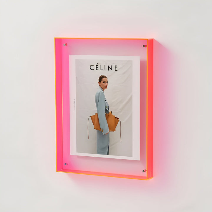 Neonroze acryl fotolijst aan een witte muur, met een modefoto van een vrouw in een lichtblauw pak met een bruine tas. 18