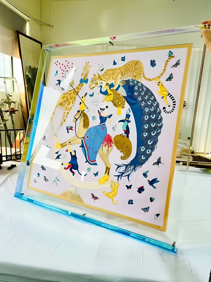Grote transparante acryllijst met blauwe rand, schuin neergezet, met daarin een kleurrijke illustratie van dieren, een pauw en een vrouw te paard. 17