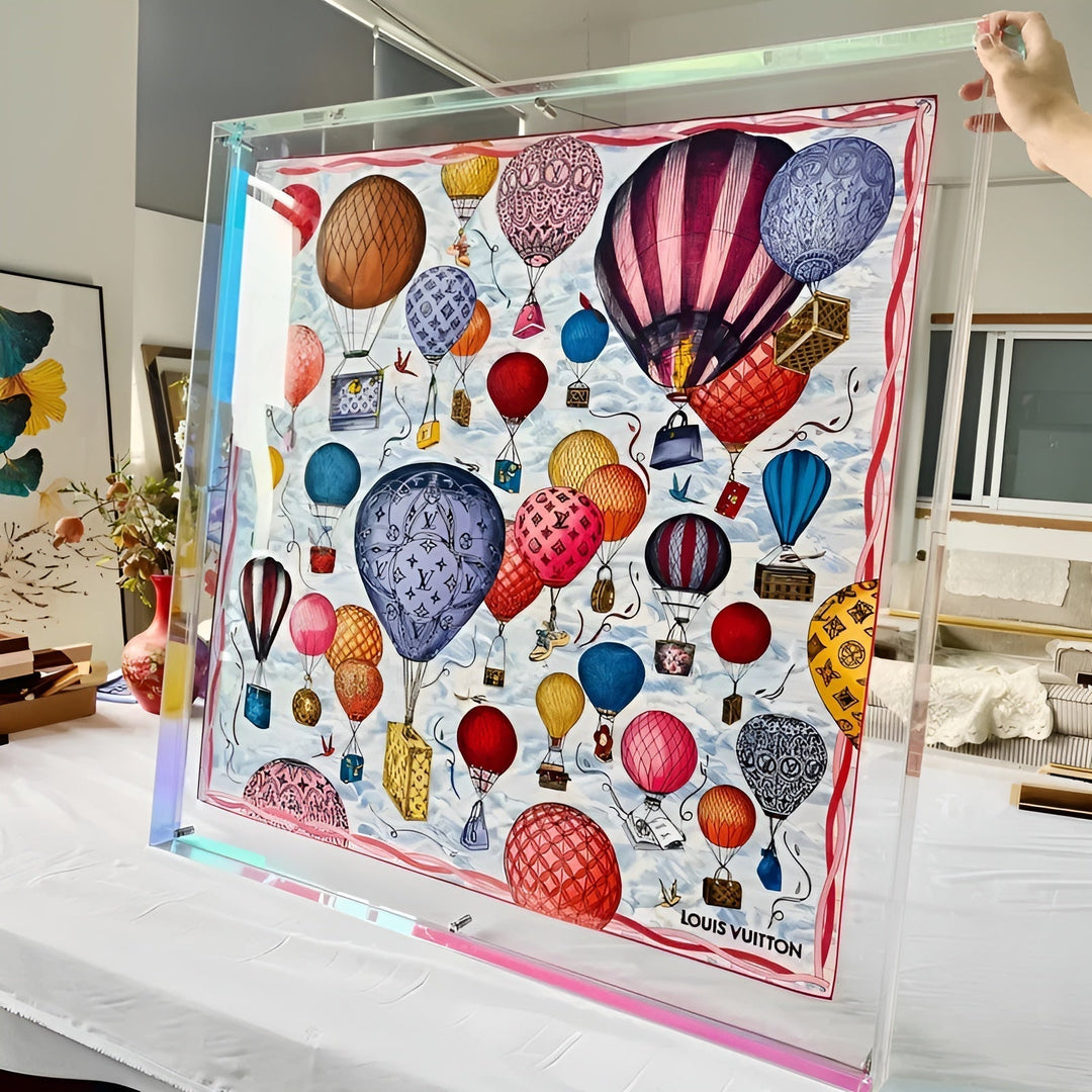 Grote doorzichtige acryllijst met regenboogkleurige neonrand, vastgehouden door een hand, met een kleurrijke print van luchtballonnen erin, op een witte tafel. 11