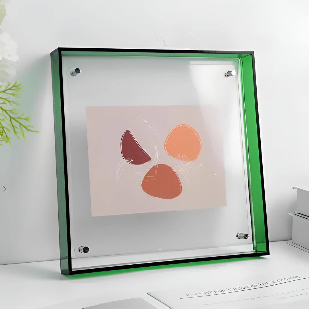 Doorzichtige acryllijst met groene rand en zichtbare bevestigingsschroefjes, schuin op een witte plank, met een abstract kunstwerk in warme oranje tinten. 21