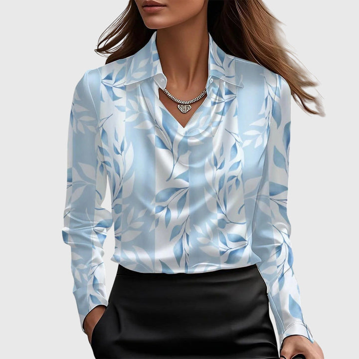 Model draagt de blouse in lichtblauw met wit bladerenpatroon, met gedrapeerde hals, kraag en een zwarte rok. 5