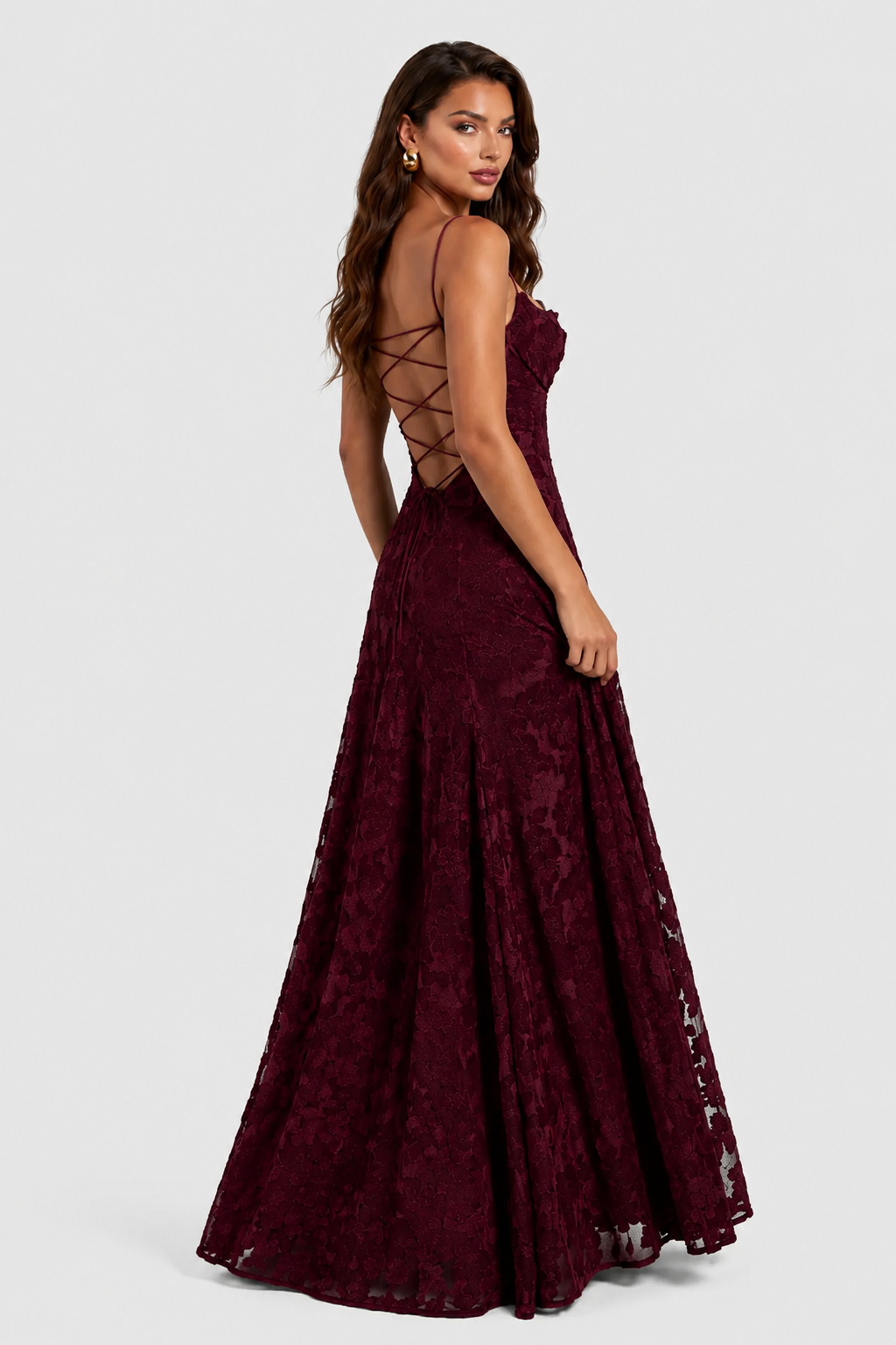 Rugzijde van de bordeauxrode jurk met gekruiste veters op de open rug, gedragen door een model dat over haar schouder kijkt. 3