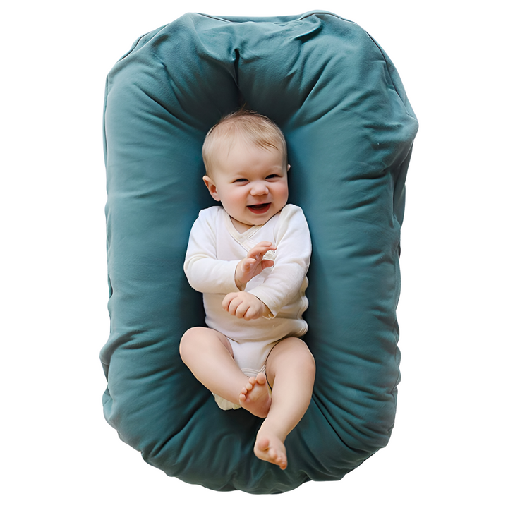 Lachende baby in witte romper ligt in een blauwgroene ligstoel, gezien van boven 2