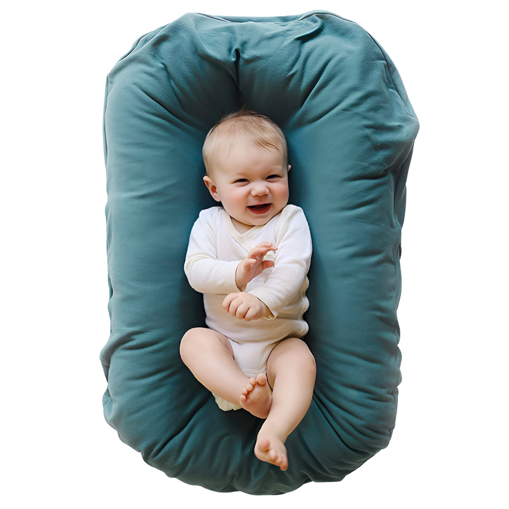 Lachende baby in witte romper ligt in een groenblauw nestje, gezien van bovenaf 2