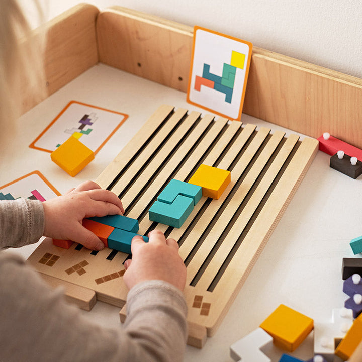 Kind legt met beide handen gekleurde blokken in de sleuven van het houten bord, met opdrachtkaarten op de achtergrond. 3