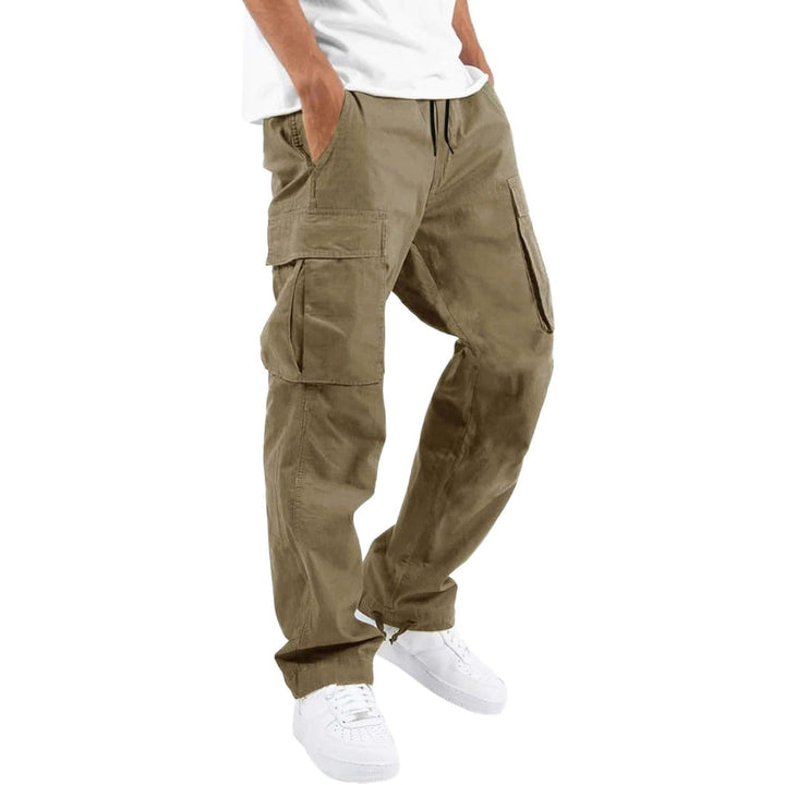 Model draagt beigebruine cargobroek met handen in de zakken, zijzakken met klep en trekkoord, gecombineerd met wit T-shirt en witte sneakers. 3