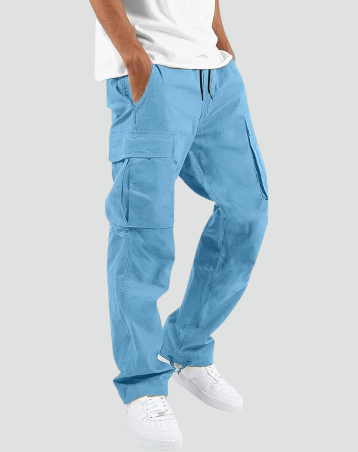 Model draagt lichtblauwe cargobroek met handen in de zakken, zijzakken met klep en trekkoord, gecombineerd met wit T-shirt en witte sneakers. 14