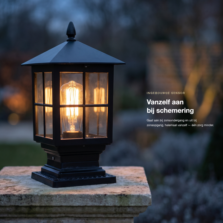 Brandende zwarte zuillamp op een stenen pilaar in de schemering, in een tuin met bewerkte promotietekst ernaast. 2