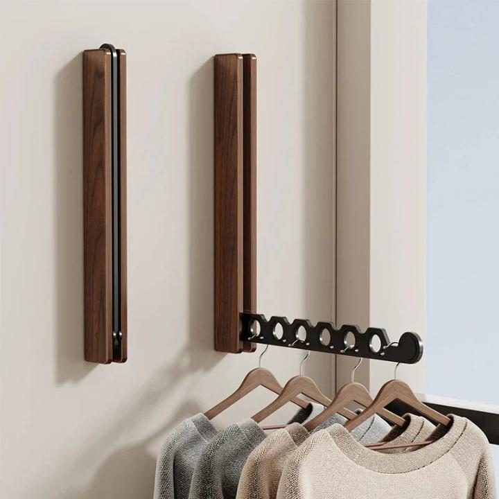 Twee donkerhouten wandkapstokken, een ingeklapt en een uitgeklapt met zwarte arm, met truien aan houten hangers eronder. 7
