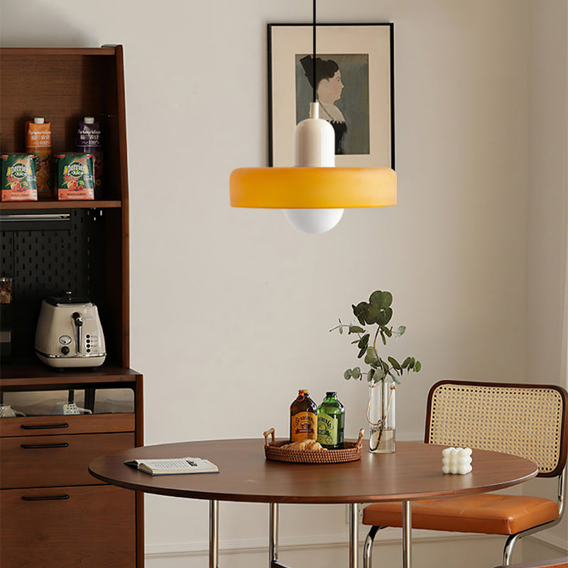 Gele glazen hanglamp met witte fitting boven een houten eettafel, met dienblad en kast op de achtergrond 31