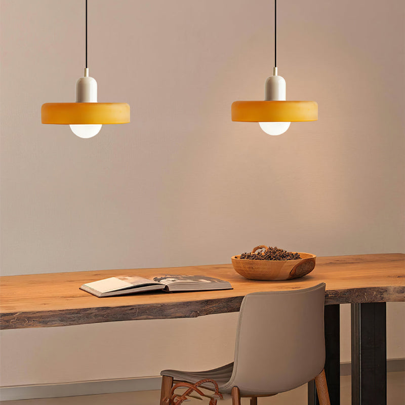 Twee oranje glazen hanglampen met witte kap boven een houten tafel met open boek en schaal 33