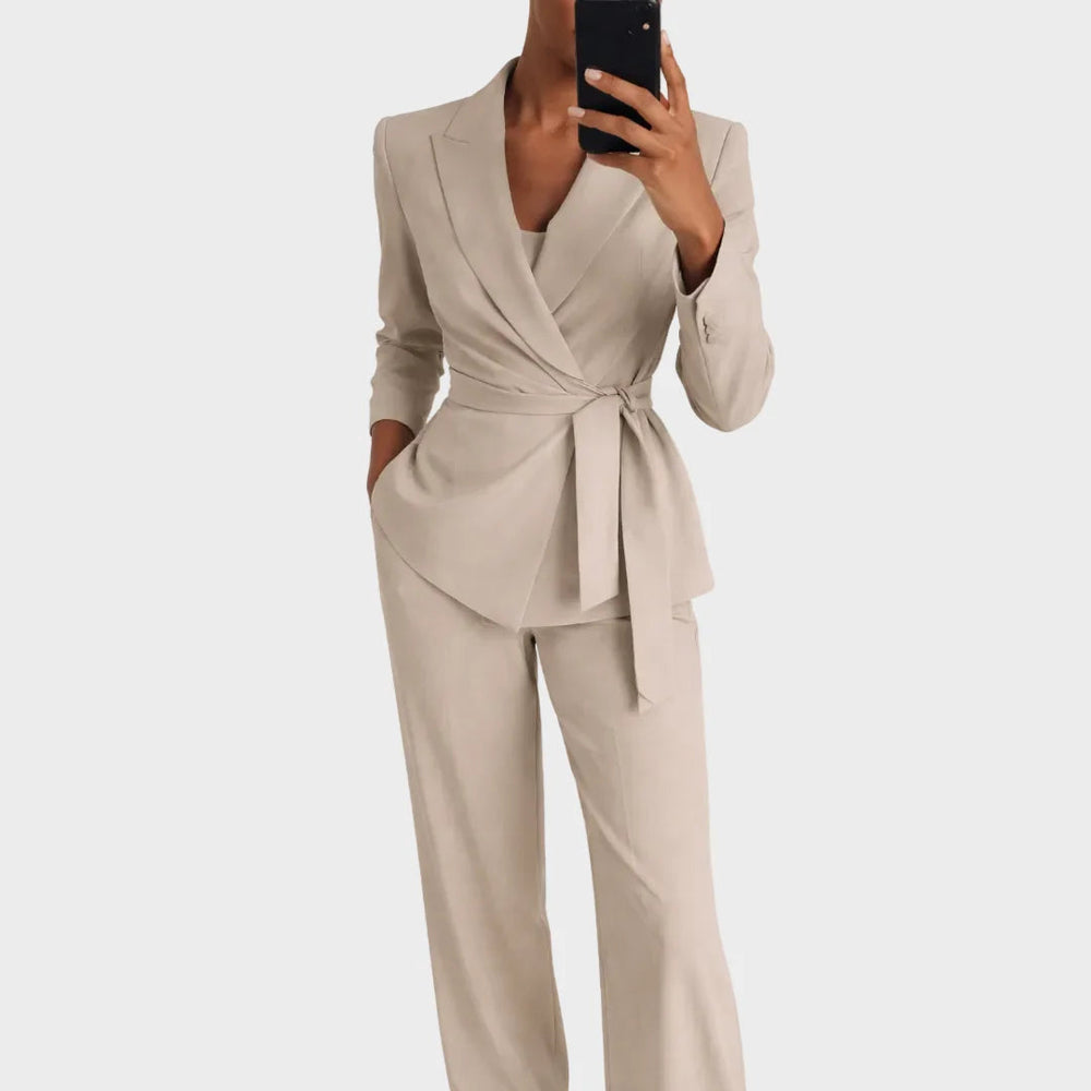 Dezelfde pakkencombinatie in beige, gedragen door een vrouw met een telefoon in haar hand, hand in de broekzak. 2