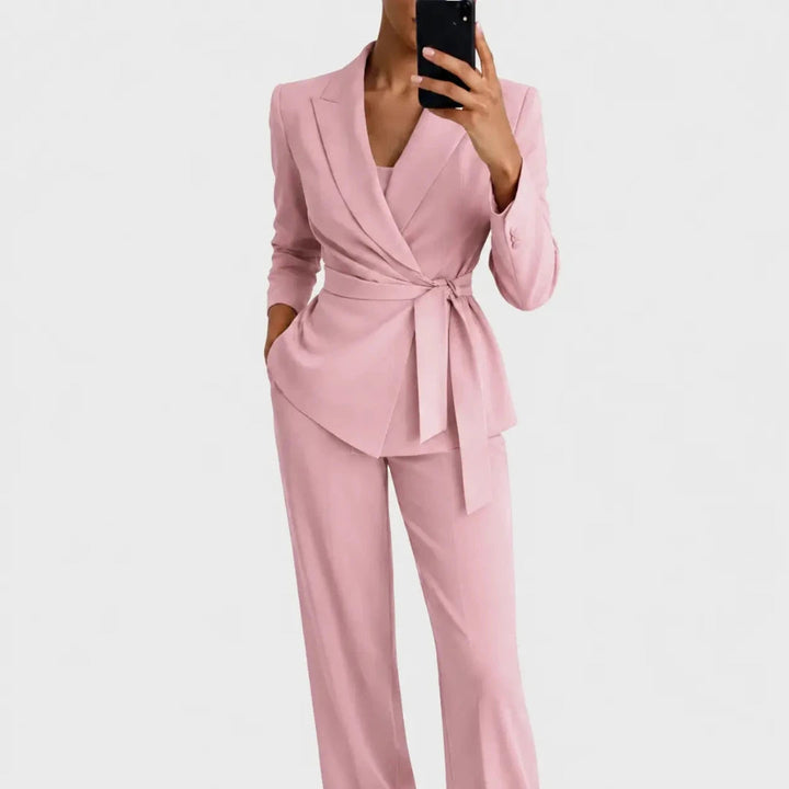 Dezelfde pakkencombinatie in roze, met blazer met overslag en geknoopte ceintuur, gedragen door een vrouw met telefoon. 4