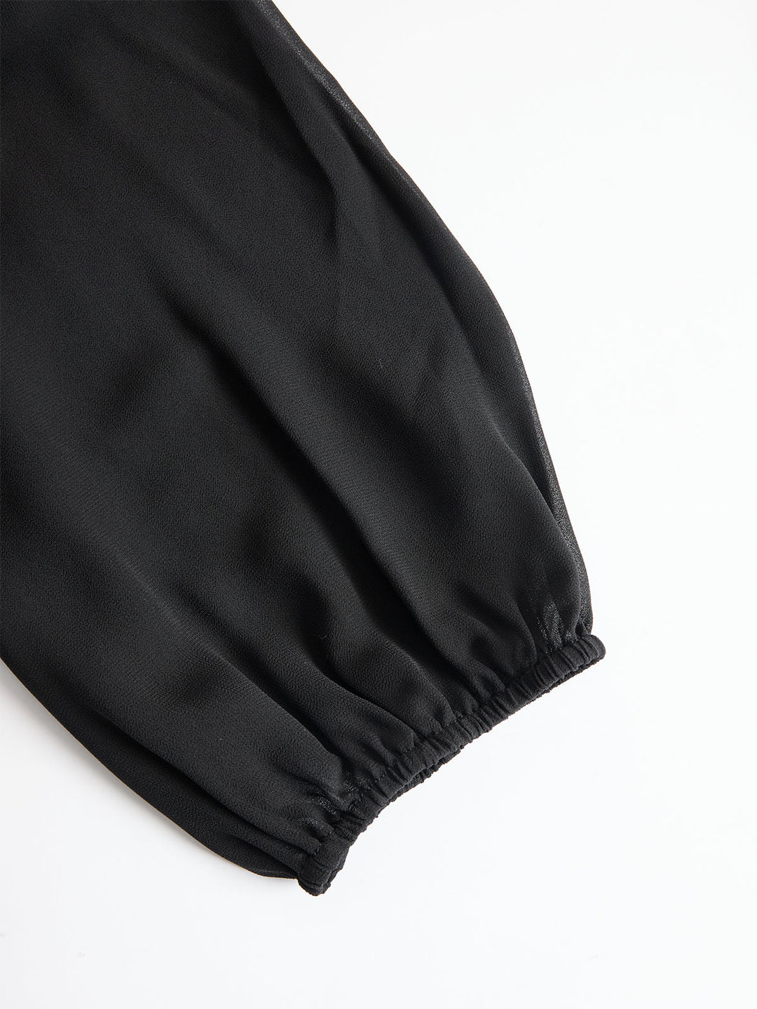 Detail van een doorschijnende zwarte pofmouw met elastische manchet, plat neergelegd op een witte achtergrond 4