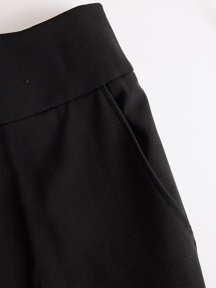 Detail van de zwarte broek met brede tailleband en steekzak, plat neergelegd op een witte achtergrond 5