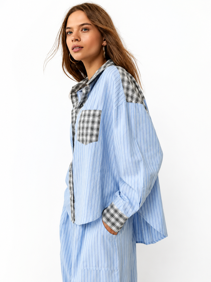 Zijaanzicht op een model in een blauw gestreept overhemd met grijs geruite schouderpartij, borstzak en manchetten, met een hand in de broekzak. 1