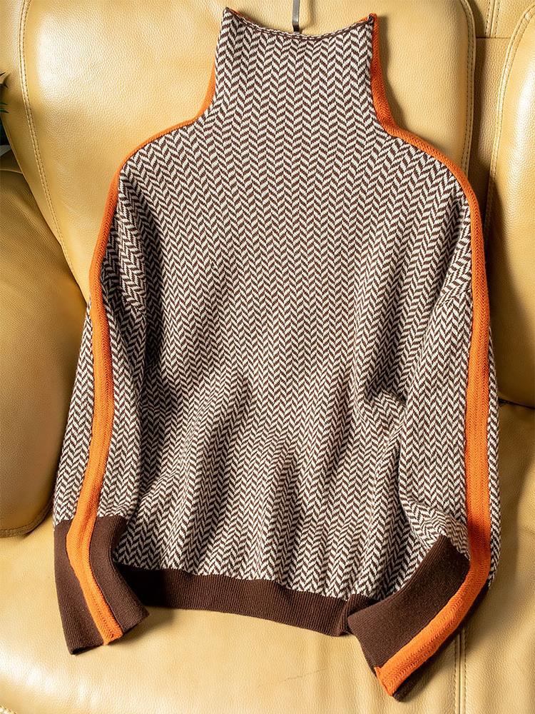 De trui plat neergelegd op een leren stoel, met visgraatpatroon, oranje zijstrepen en bruine boorden aan mouwen en onderrand. 4