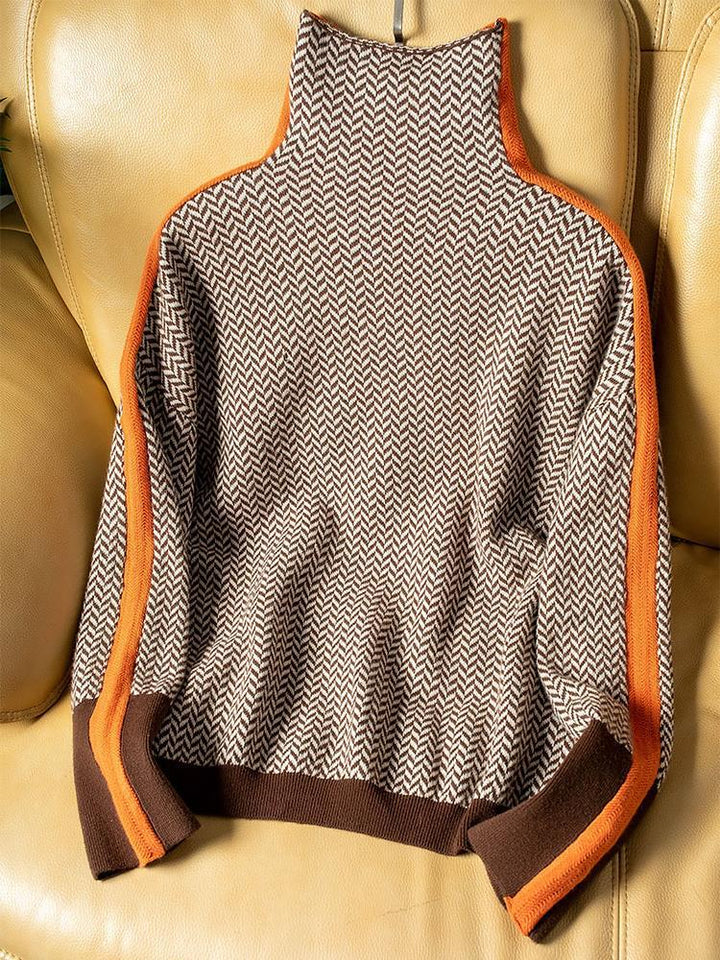 De trui plat neergelegd op een leren stoel, met visgraatpatroon, oranje zijstrepen en bruine boorden aan mouwen en onderrand. 4