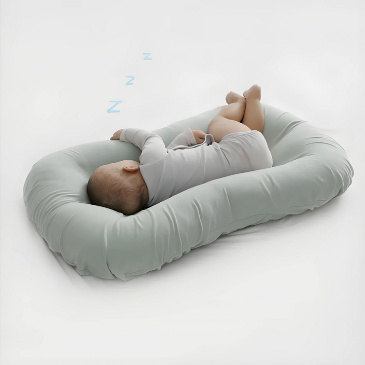 Slapende baby in grijze romper ligt op zijn zij in een lichtgroen kussen 3