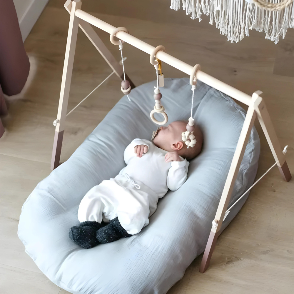 Baby in blauwgrijs kussen onder een houten speelboog met hangende speeltjes 6