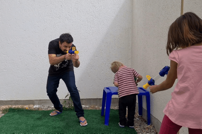 Man en twee kinderen spelen buiten op een grasmat met blauwgele speelgoedpistolen 9