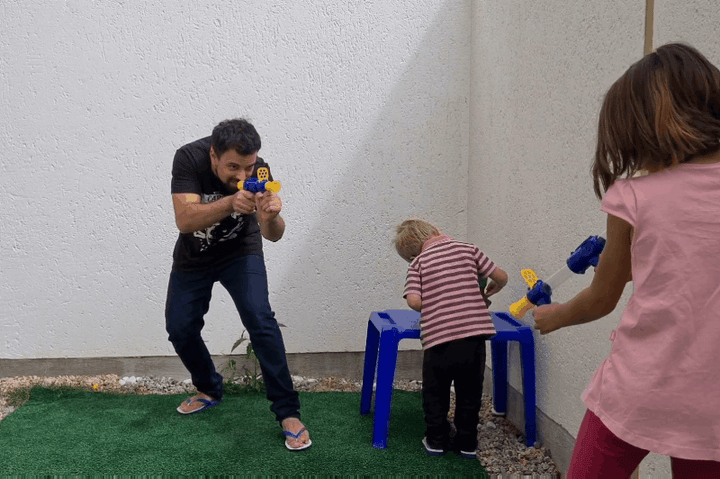 Man en twee kinderen spelen buiten op een grasmat met blauwgele speelgoedpistolen 9