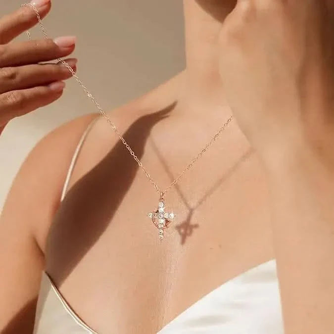 Vrouw in witte top houdt een fijne ketting met kruishanger met kleine steentjes omhoog, de hanger werpt een schaduw op haar huid. 1