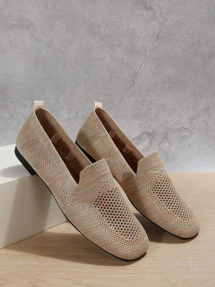 Beige gebreide instapschoenen met open mesh en hielband, schuin tegen een wit blok geplaatst voor een grijze betonnen muur. 7