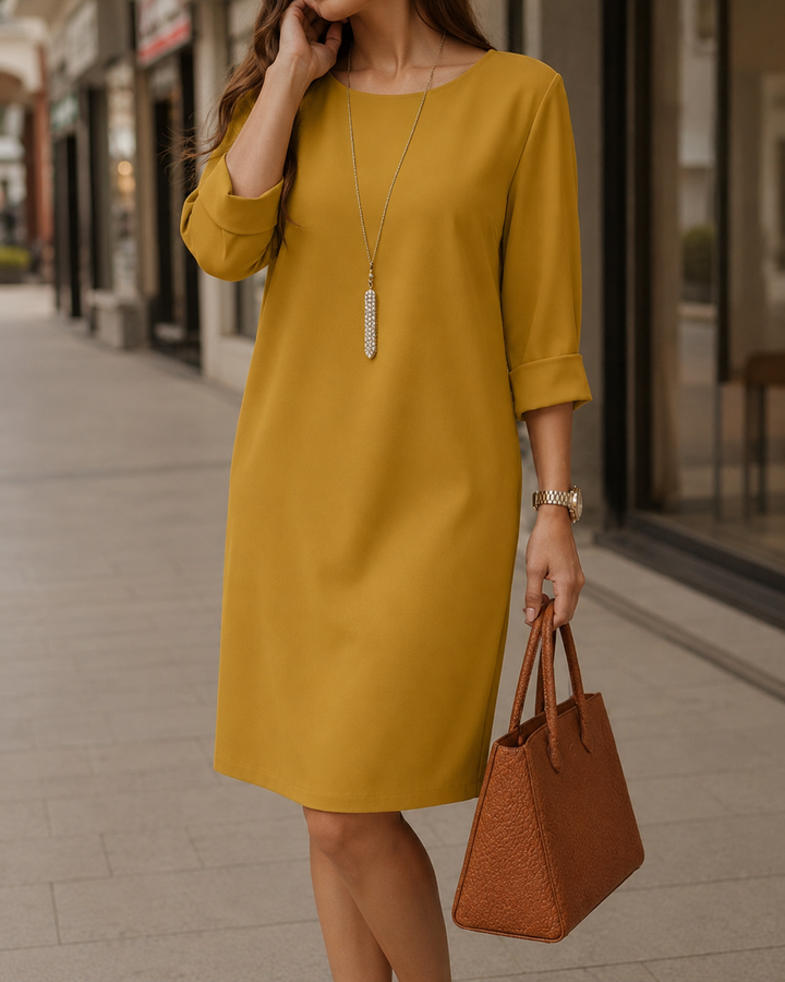 Mosterdgele jurk met omgeslagen mouwen, model op straat met lange ketting, horloge en bruine handtas 7